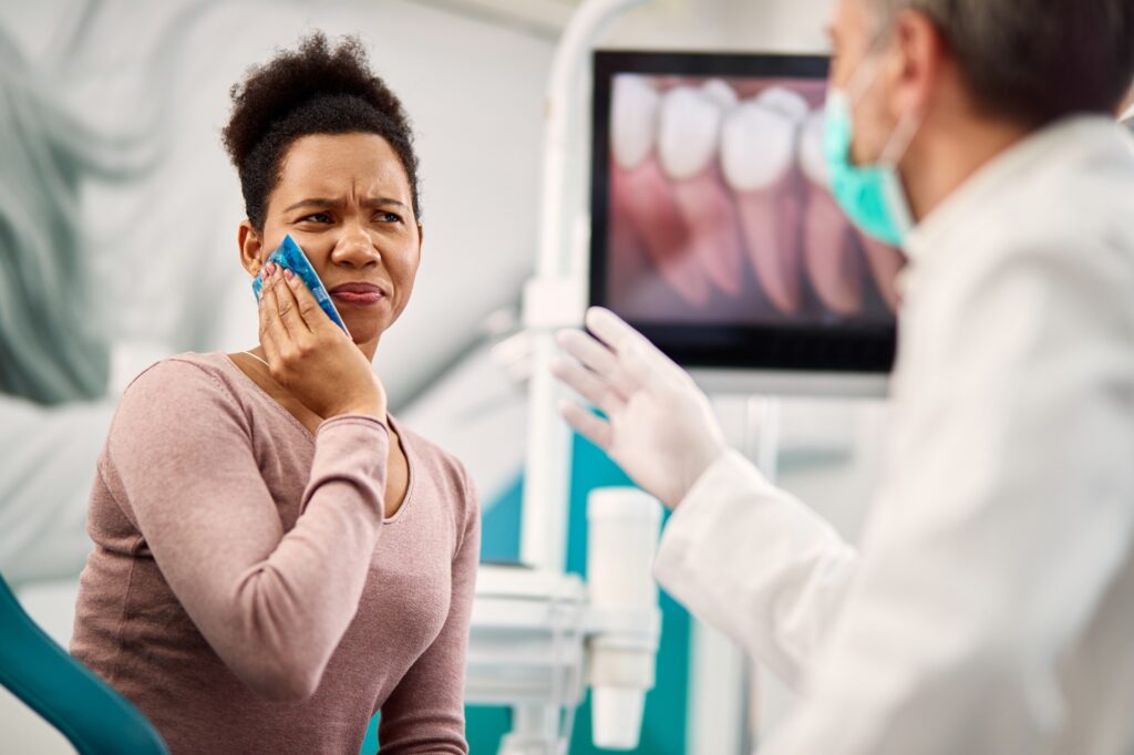 Patient in Kenmore WA holding cheek in pain while dentist examines tooth for emergency dental issue